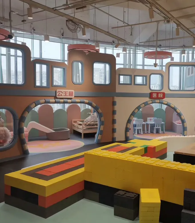صالة العاب داخلية للأطفال تحتوي على مجسمات تشبه المنازل الصغيرة وألعاب تعليمية، مع ألوان مثل الوردي والأزرق ومقاعد وطاولات مخصصة للأطفال