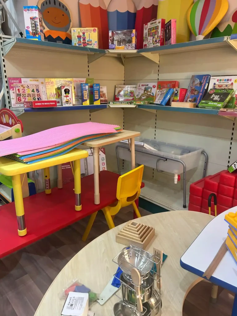 زاوية داخل تجهيزات روضات الأطفال تحتوي على طاولات وكراسي صغيرة ملونة وألعاب تعليمية وكتب وأنشطة تنمية المهارات معروضة على الرفوف