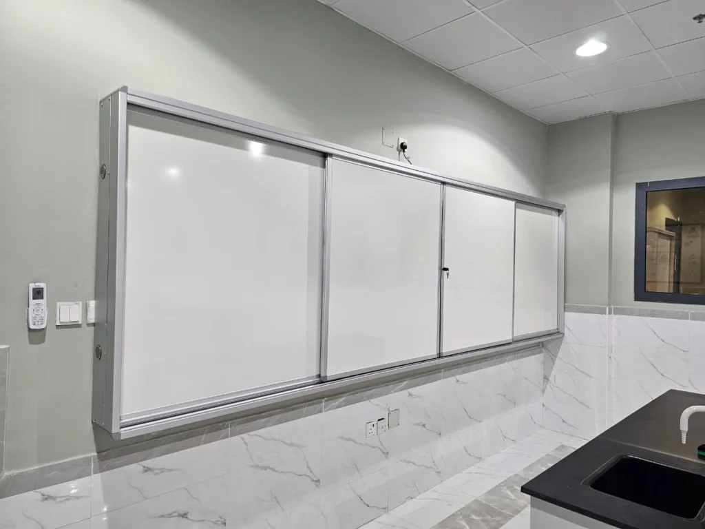 سبورة بيضاء منزلقة بإطار من الألمنيوم مثبتة على جدار فصل دراسي حديث بتشطيب رخامي وأرضية لامعة