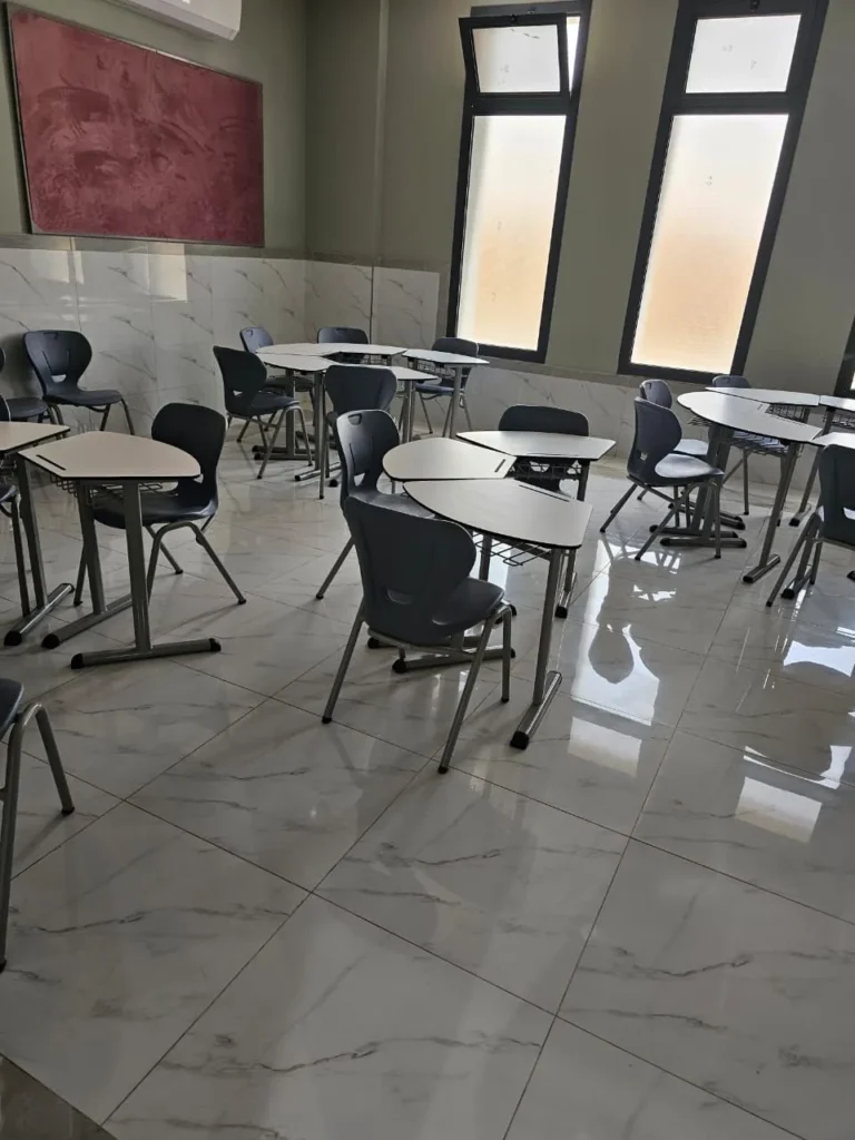كراسي وطاولات المدارس مرتبة داخل فصل دراسي مضاء طبيعياً ومجهز بتصميم عصري